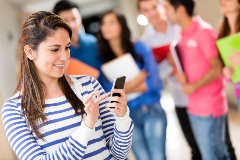Students walk in a hallway and the main student is on her phone